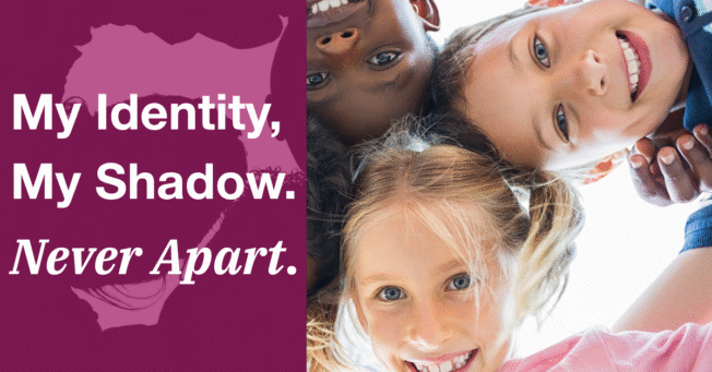 Image of children in a circle, smiling at the camera below, with the caption "My Identity, My Shadow. Never Apart."