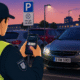 The image shows a public order office employee scanning the license plate of an unlawfully parked vehicle with his mobile phone.